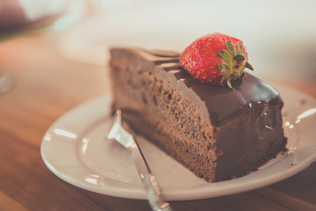 Slice of chocolate cake topped with a strawberry on a white plate with a fork next to it