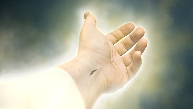Left hand outstretched with white sleeve at wrist, a nail mark in the wrist and in the hand, and a glow around the entire body part.