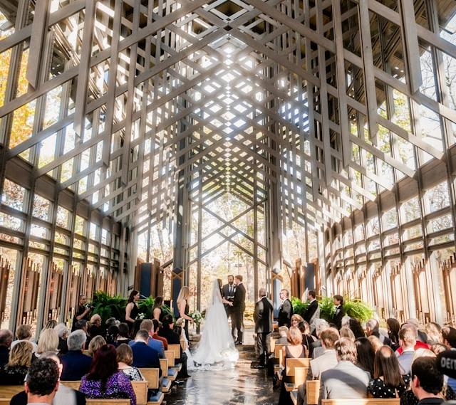 Wedding with bride and groom facing each other in Thorncrown Chapel with wedding guests filling the pews