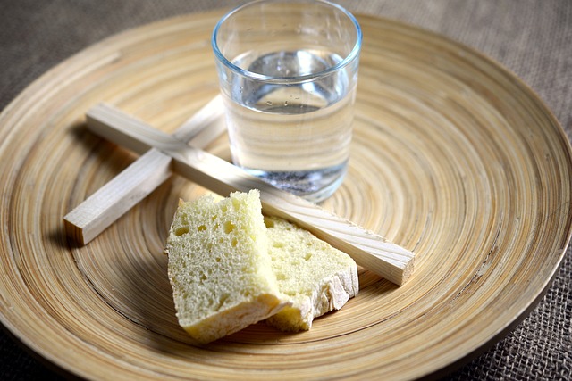 Plate with wooden cross, glass of water, and 2 small pieces of bread on it