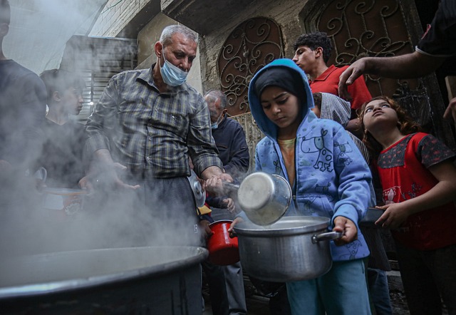 Older man standing behind massive kettle distributing food to kids in Gaza