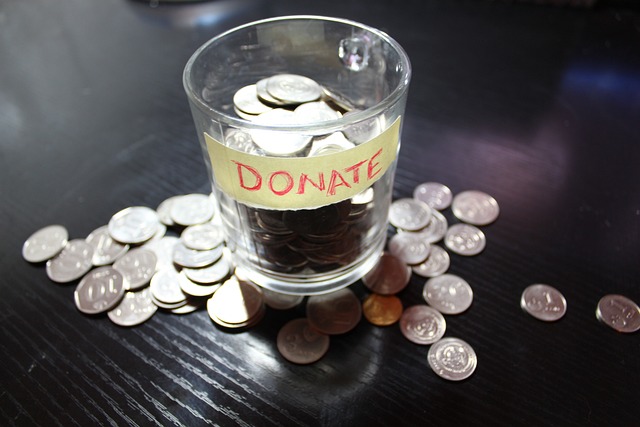 Glass cup with label marked "DONATE" sitting on a table surrounded by coins