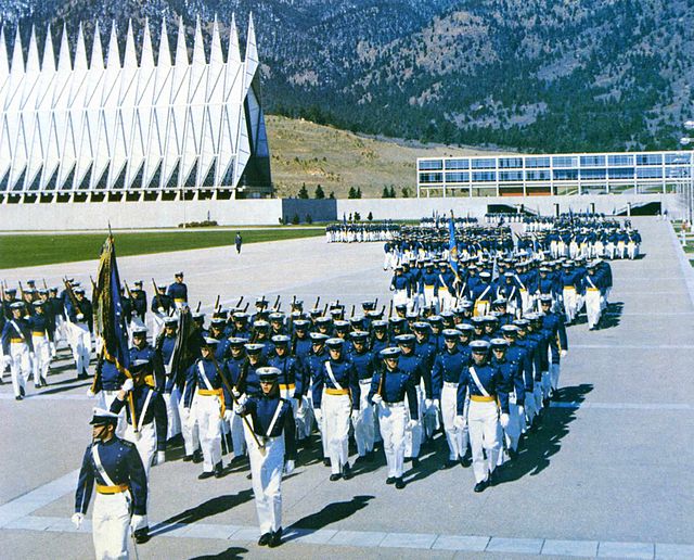 Uniformed cadets march in the cadet area with the Cadel Chapel and mountains in the background