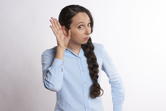Young woman in light long-sleeve shirt with her hand up to her ear as if listening