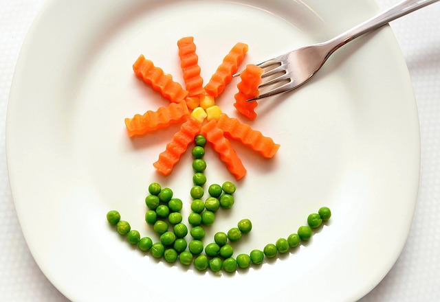 White plate with carrots and peas in the shape of a flower with fork resting on top right hand side of the plate