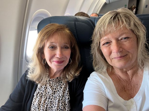 Two smiling women sitting side by side in seats on plane