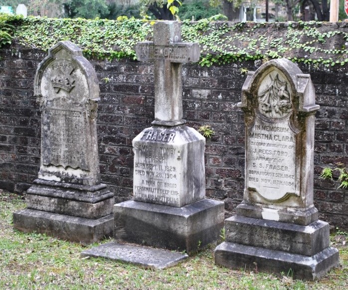 Headstones of three graves sitting side by side in front of an old brick wall