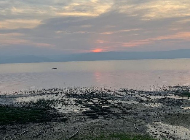 View of Sea of Galilee from the shore with clouds in the sky and the sun beginning to rise