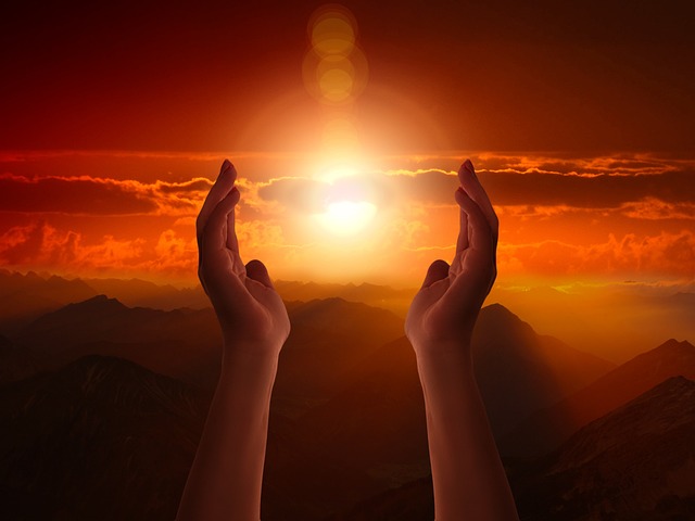 Image of two hands raised towards an orange sky with the sun in between them