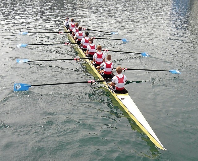 Back view of 8+ rowing crew in a shell in the water with oars extended