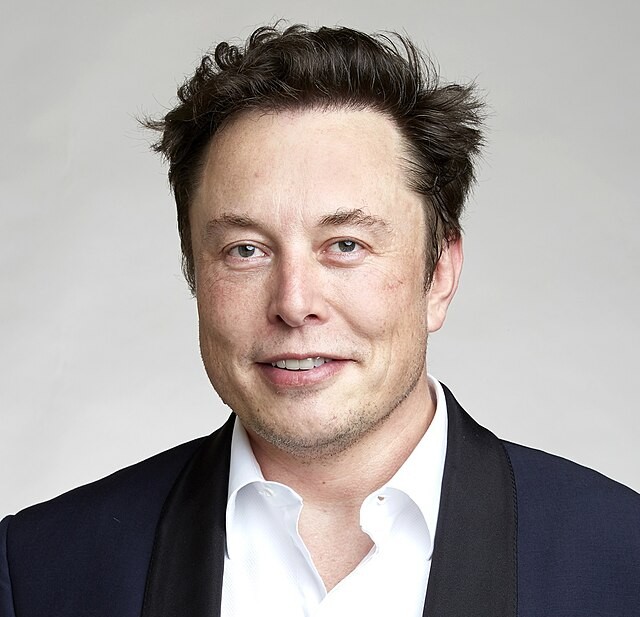 Elon Musk pictured from the shoulders up wearing a dark jacket and a white, collared button-up shirt
