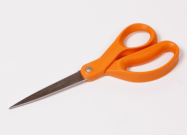 Pair of large scissors with orange handles against a light background
