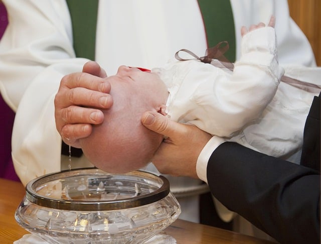 Close up shot of baby head being held over crystal bowl of water for baptism with hand of priest in white robe on child's head