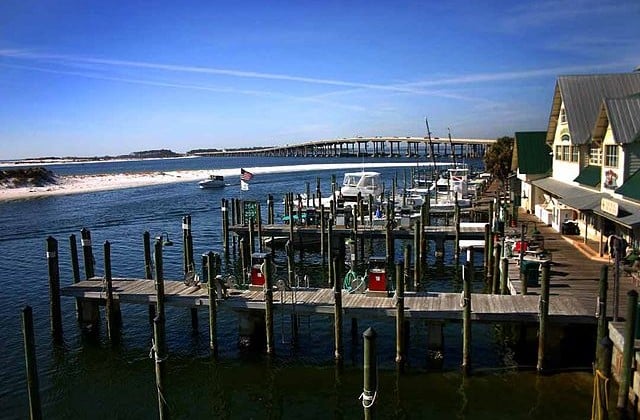 View of the Destin Marina with docks on front and blue water, white sand, and a bridge in the background