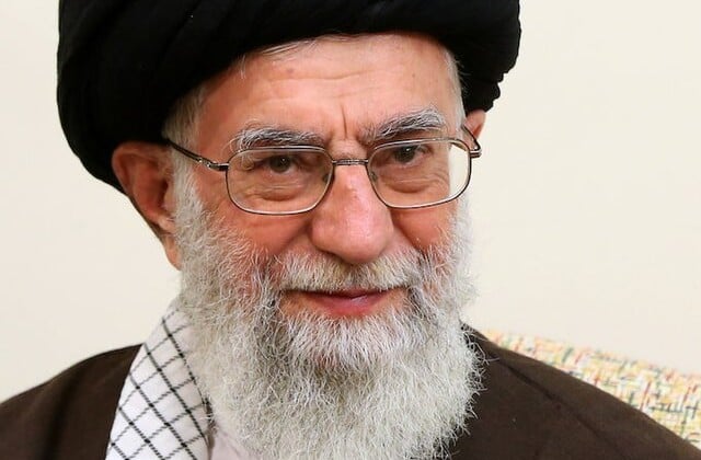 Facial view of older man with wire-rimmed glasses and a long white beard wearing a dark head covering