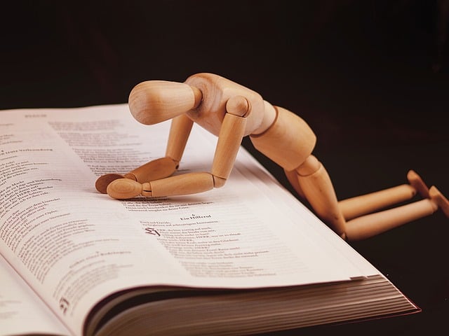 Small wooden doll figure kneeling in prayer with hands clasped in prayer resting on Bible page
