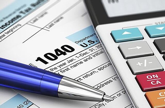 A pen and a calculator resting on top of a 1040 tax form