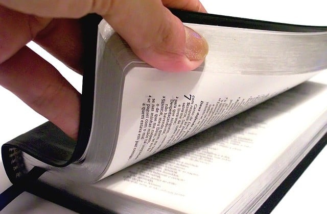 Close-up of left hand lifting cover of Bible lying on flat surface