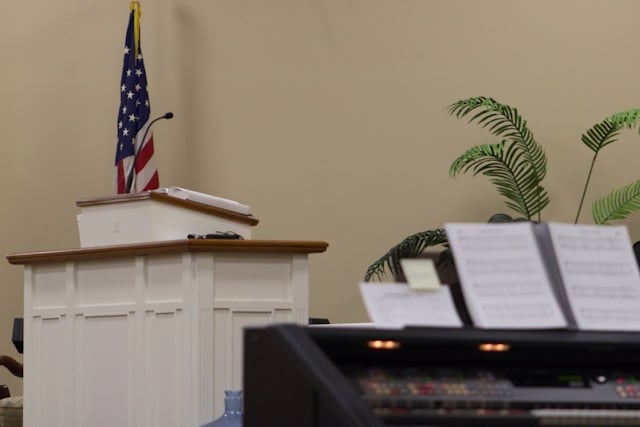 View towards white church pulpit with microphone with American flag in the background and top of organ in front of it