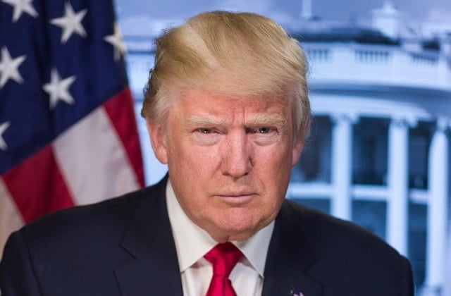 Headshot of Pres. Donald Trump in a white shirt and red tie with the American flag and the White House partially shown in the background