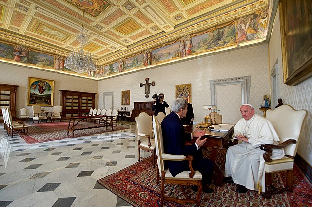 View of large area in papal apartment with Pope Francis and US Secretary of State John Kerry seated in chairs and speaking to each other