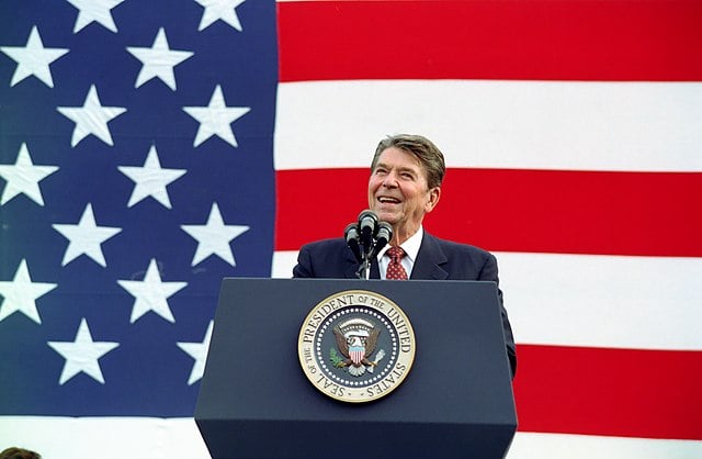 Pres. Ronald Reagan speaking at a podium in front of a US flag backdrop