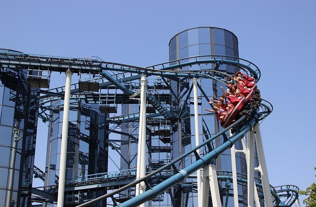 View of roller coaster car full of riders with their hands in the air coming around a steep curve and headed down the track.