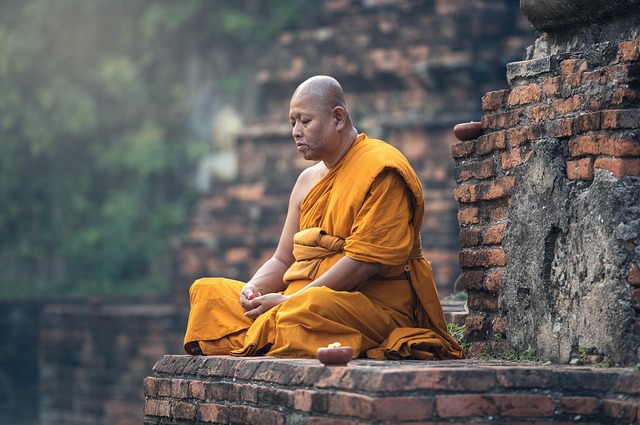 Buddhist monk in a saffron robe sitting cross-legged on a stone structure