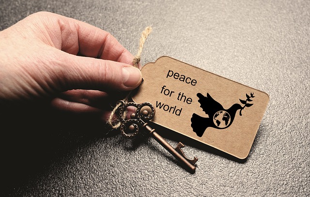 Fingers of left hand holding an old-fashioned key to which is attached a rectanguler item saying, "peace for the world"