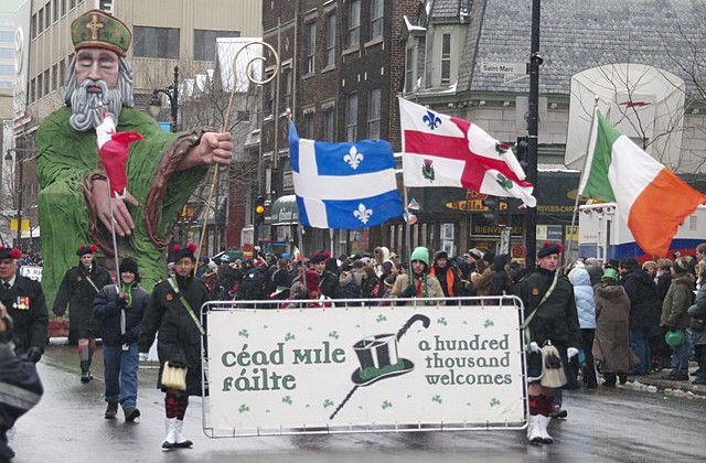 Marchers in St. Patrick's Day Parade going down city street holding a banner and flags