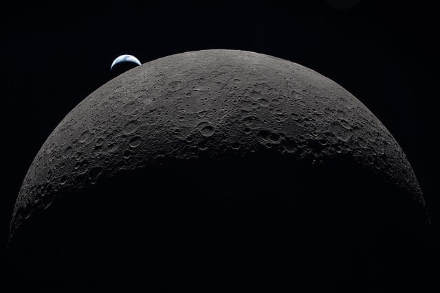 View of dark side of the moon with draters visible and the Earth setting in the top lefthand corner above it