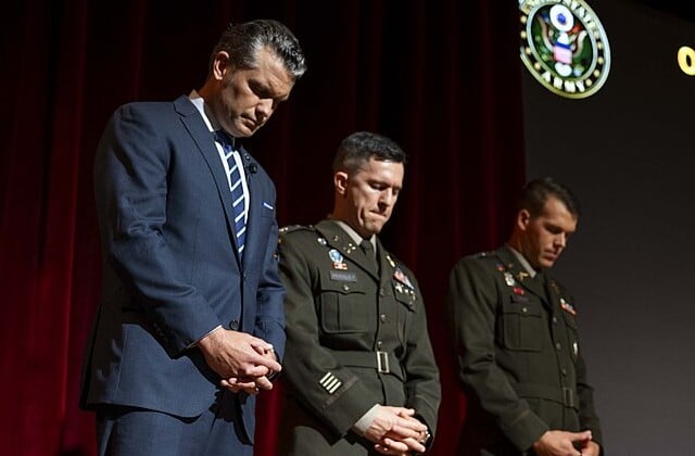Defesne Secretary Pete Hegseth in a suit and tie bows in prayer next to two Army officers in uniform
