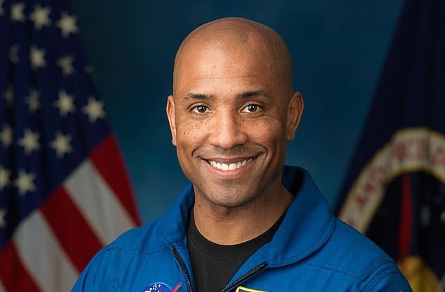 Head shot of black astronaut Victor J. Glover smiling posed with US flat behind him to the side