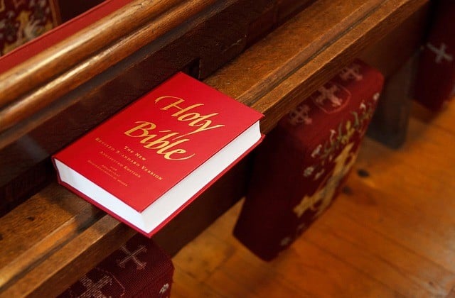 Red bible with gold lettering on cover lying on rail in church