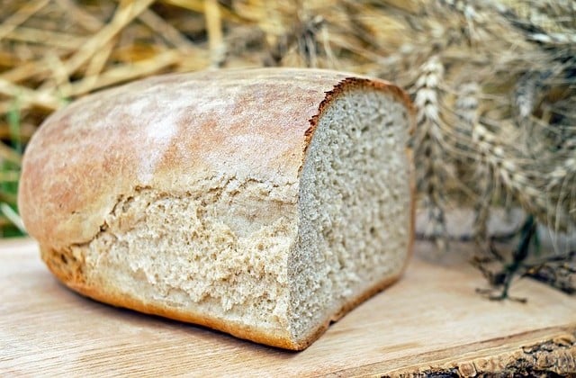 Half a loaf of unsliced bread sitting on a light colored surface with wheat in the background