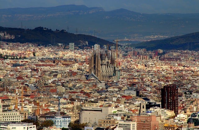 View down on city of Barcelona with mountains in the distance and church Sagrada Familia tower over surrounding structures