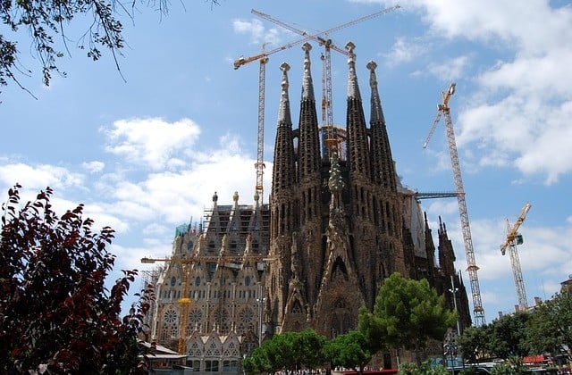 Exterior view of church under construction with several cranes seen around and above the spires