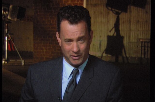 Front view of actor Tom Hanks in a dark gray suit and tie seen from the chest up.