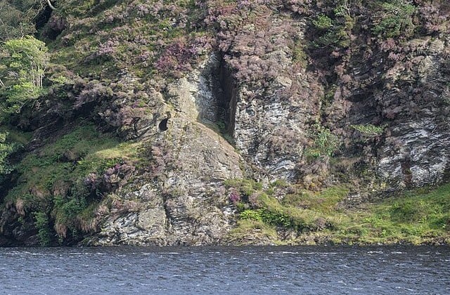 View across lake to small cave opening up on the rocky mountain side.
