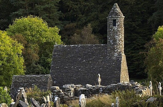 Side view of medieval stone church with round bell tower and gravetones outside the church.