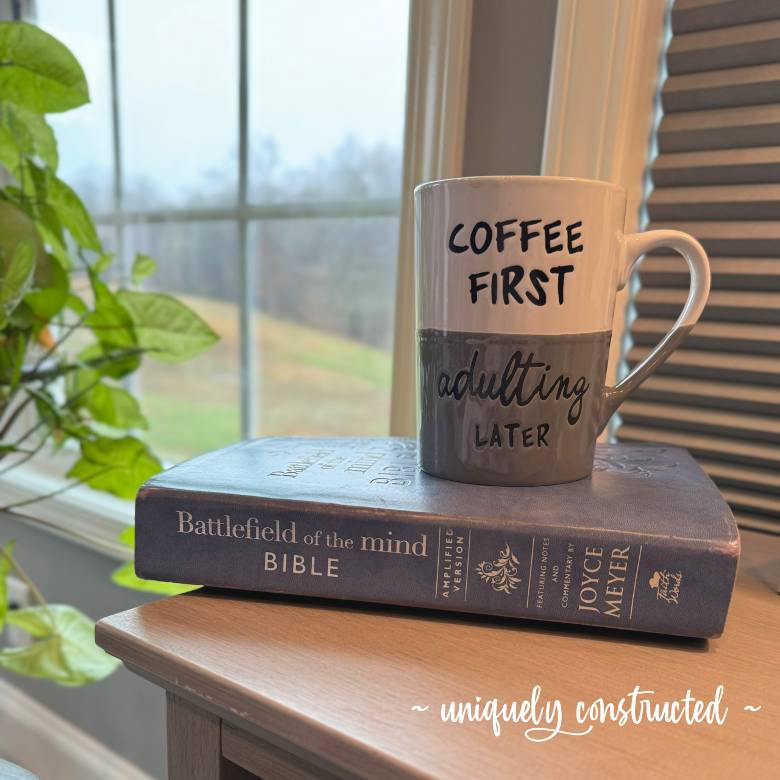 A Bible with a coffee mug that says coffee first, adulting later