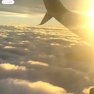 Photo looking out of airplane window, sunrising, and white puffy clouds!