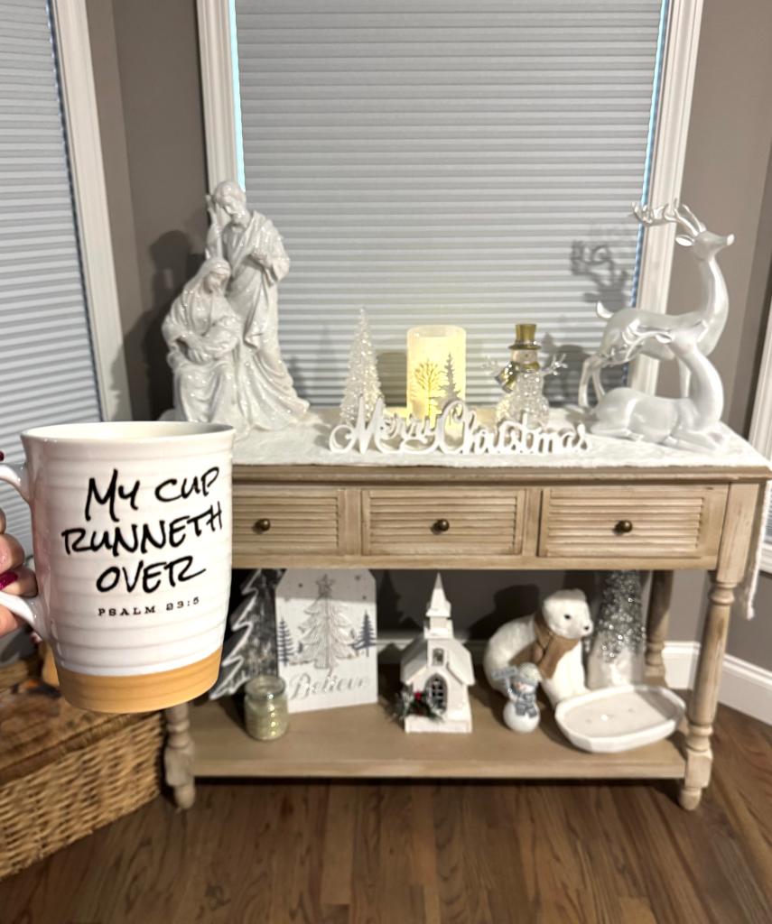 Coffee mug with slogan: my cup runneth over and Christmas decor that includes a Joseph, Mary and baby Jesus statue.
