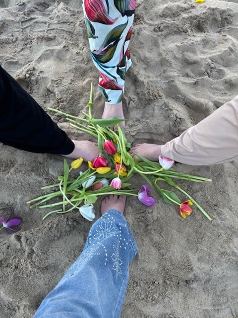 Women's feet in the sand with beautiful flowers added to the mix.
