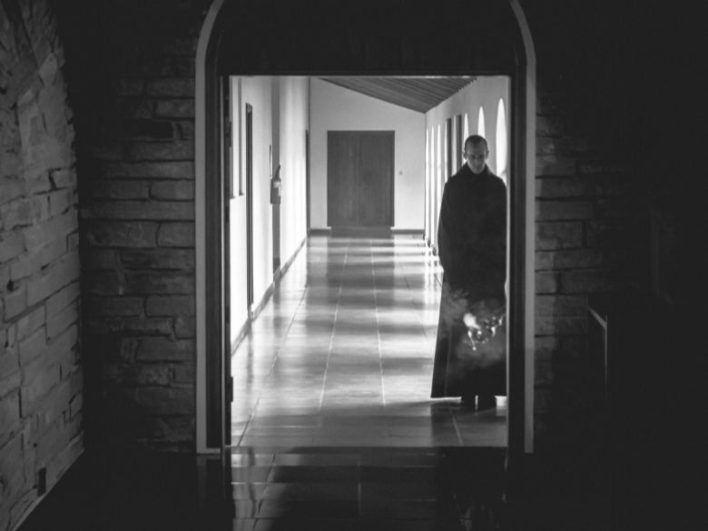 A Monk, understanding the benefits of silence, stands in the hallway of a monastery.