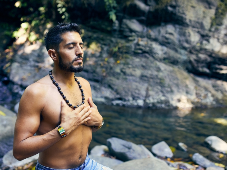 A man seated in meditation with his hands placed over his heart chakra