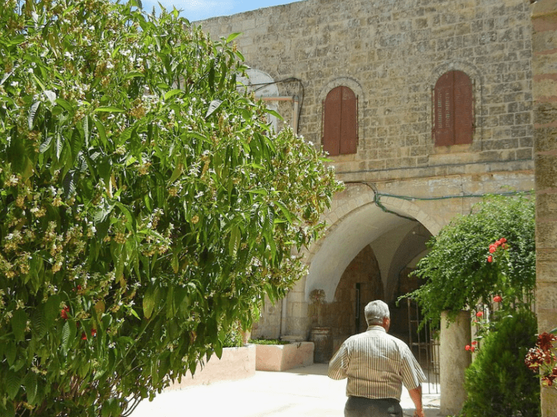 Image of the monastery and church with a bush in the foreground and a man walking away from the camera