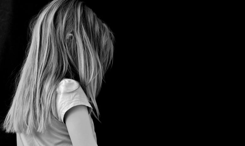 A young child with long hair viewed from the side and back against a dark background.
