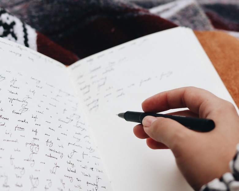 Woman wrapped in a blanket with fountain pen writing in a paper journal. The featured image for 8 Easy Exercises to Journal About Your Heart by Mark Whitlock on Patheos.