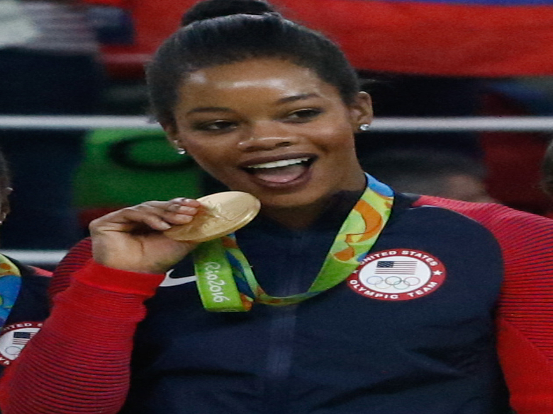 Gabby Douglas clinching and playfully biting the gold medal she won at the 2016 Rio Olympics.